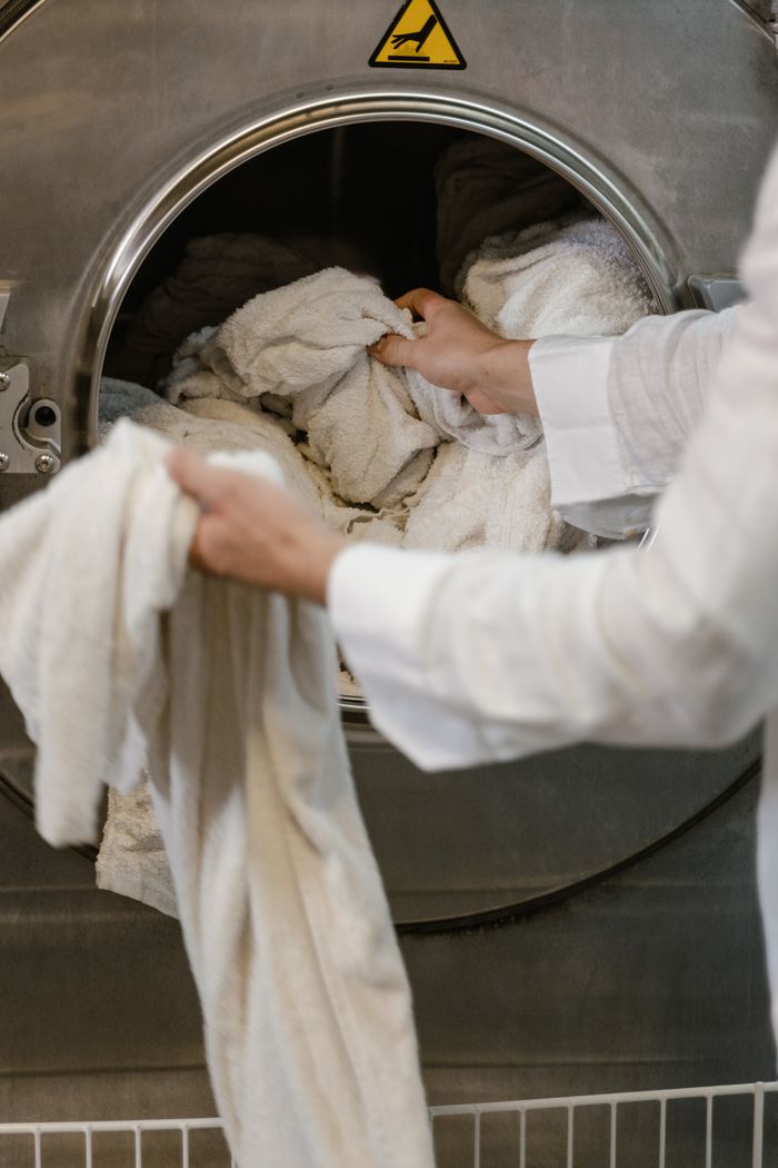 why-choose-us A person loading towels into an industrial washing machine in a launderette.