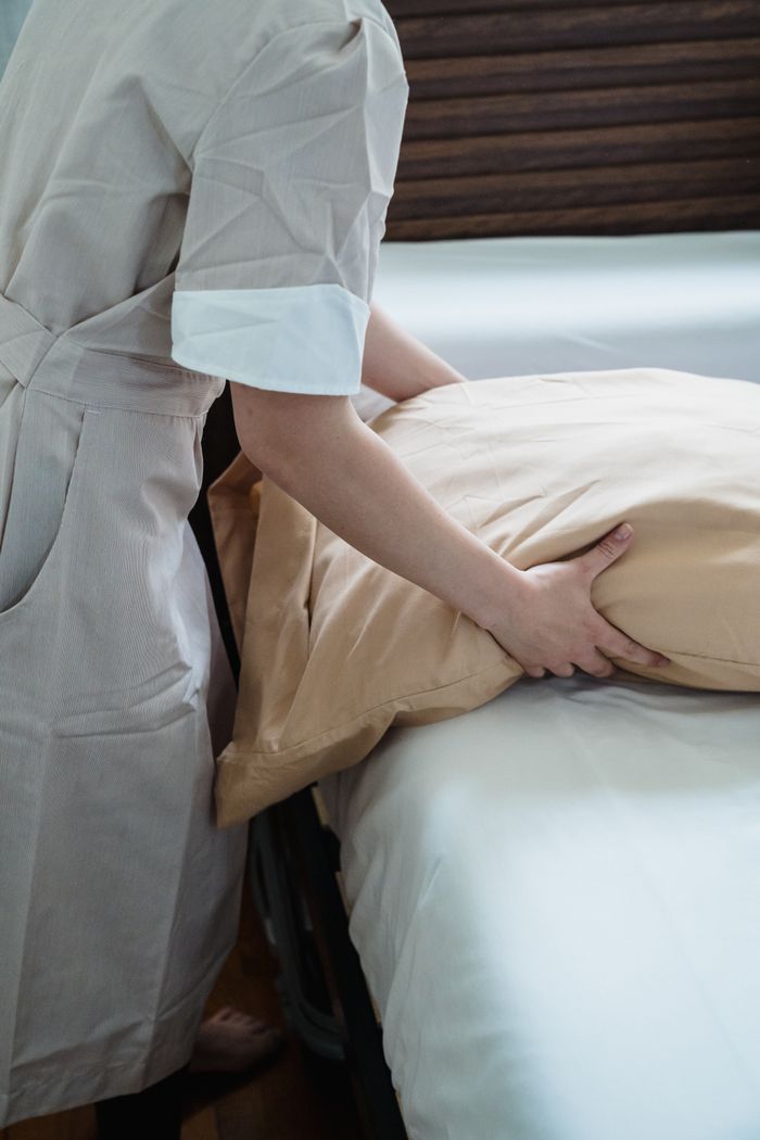 Services-02 Hotel staff adjusting a pillow on a bed, ensuring guest comfort in a cozy room.